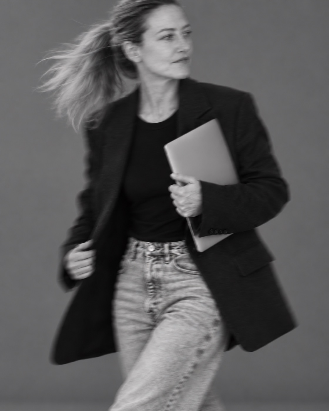 Kate walking with a laptop under her arm, in black and white